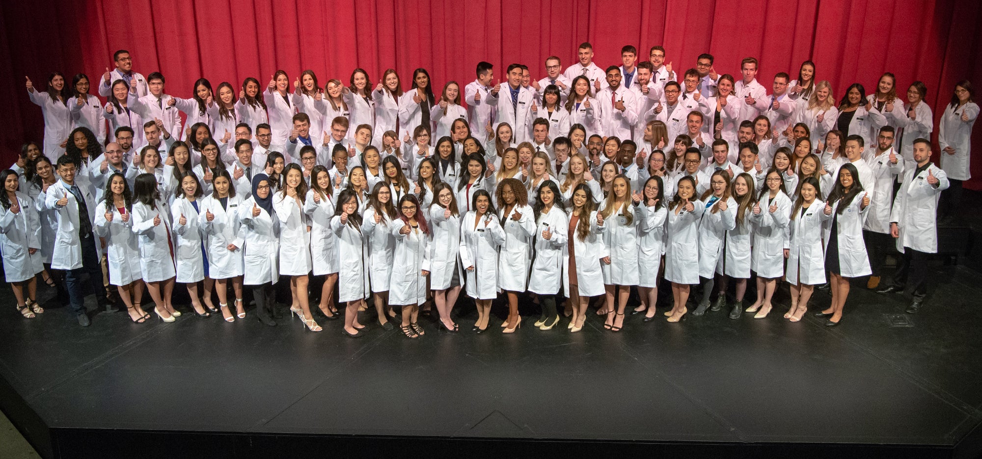 Class of 2022 in their white coats giving thumbs up
