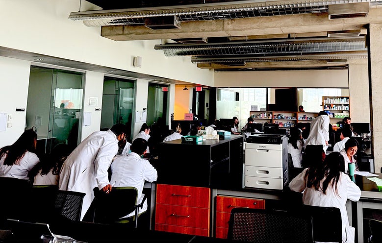 Students in a lab in white coats sitting in groups working together