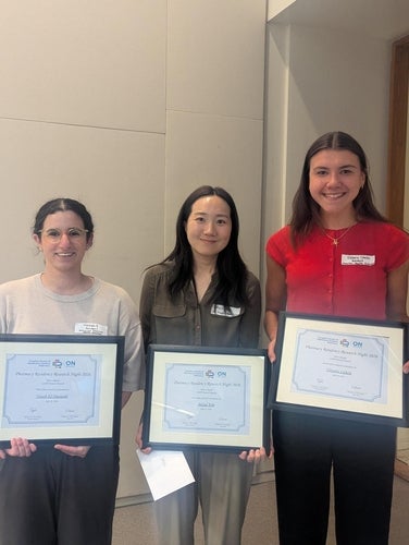 Three individuals pose indoors while holding framed certificates recognizing achievements at the 2026 Pharmacy Residency Research Night. The recipients stand side by side in front of a neutral wall, each displaying an award certificate in a black frame.