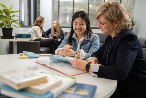 a student and faculty member look at textbooks on a desk