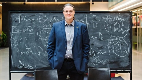 Avery Broderick standing in front of a chalkboard displaying his research.