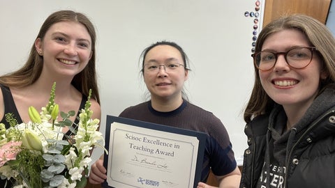 Brenda Lee holding her award and flanked by two students.