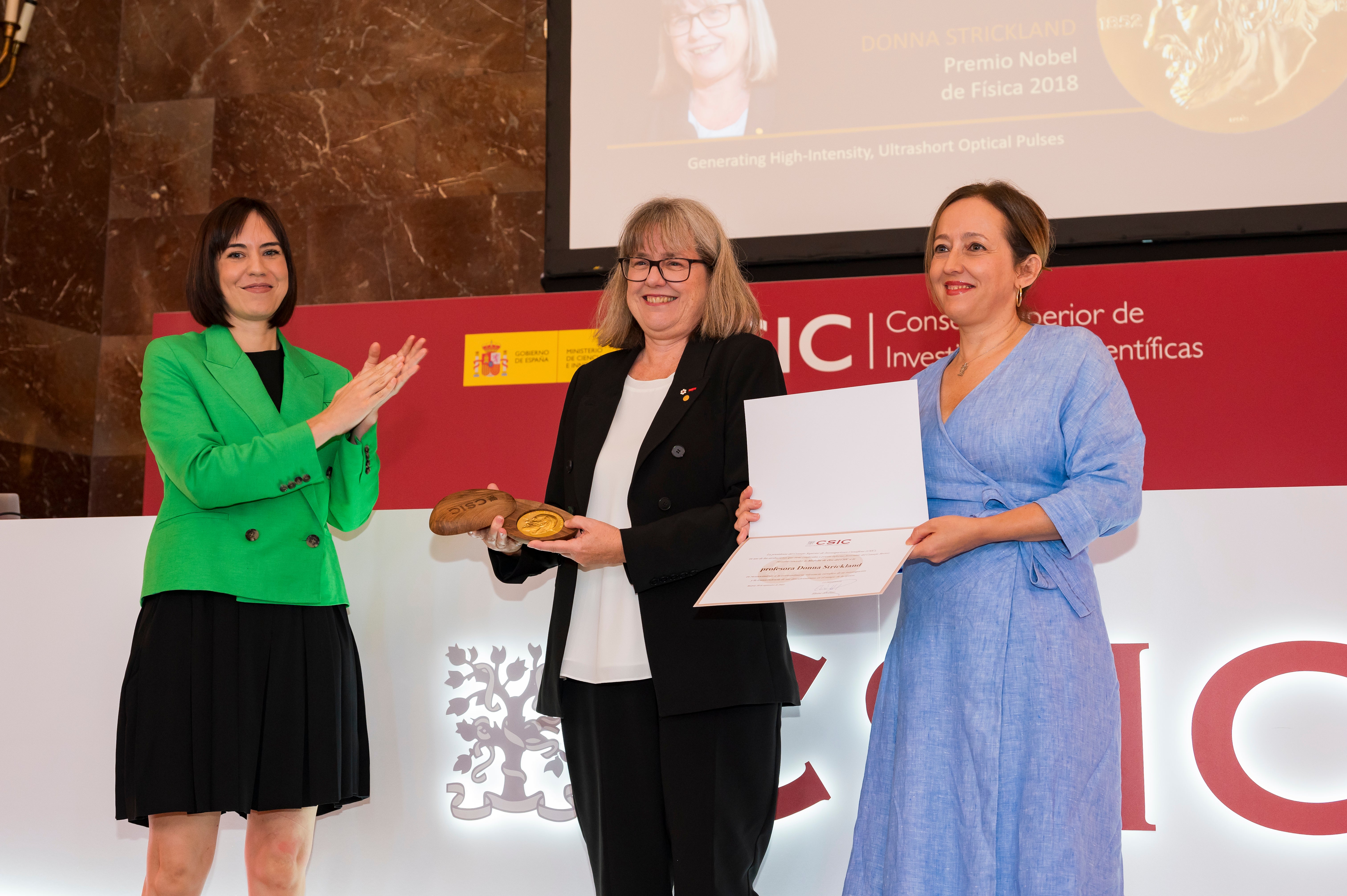 Image of Noble Prize Winner, Donna Strickland, receiving  Gold Medal from the acting minister of science and innovation, Diana Morant, and the president of the CSIC, Eloisa del Pino.