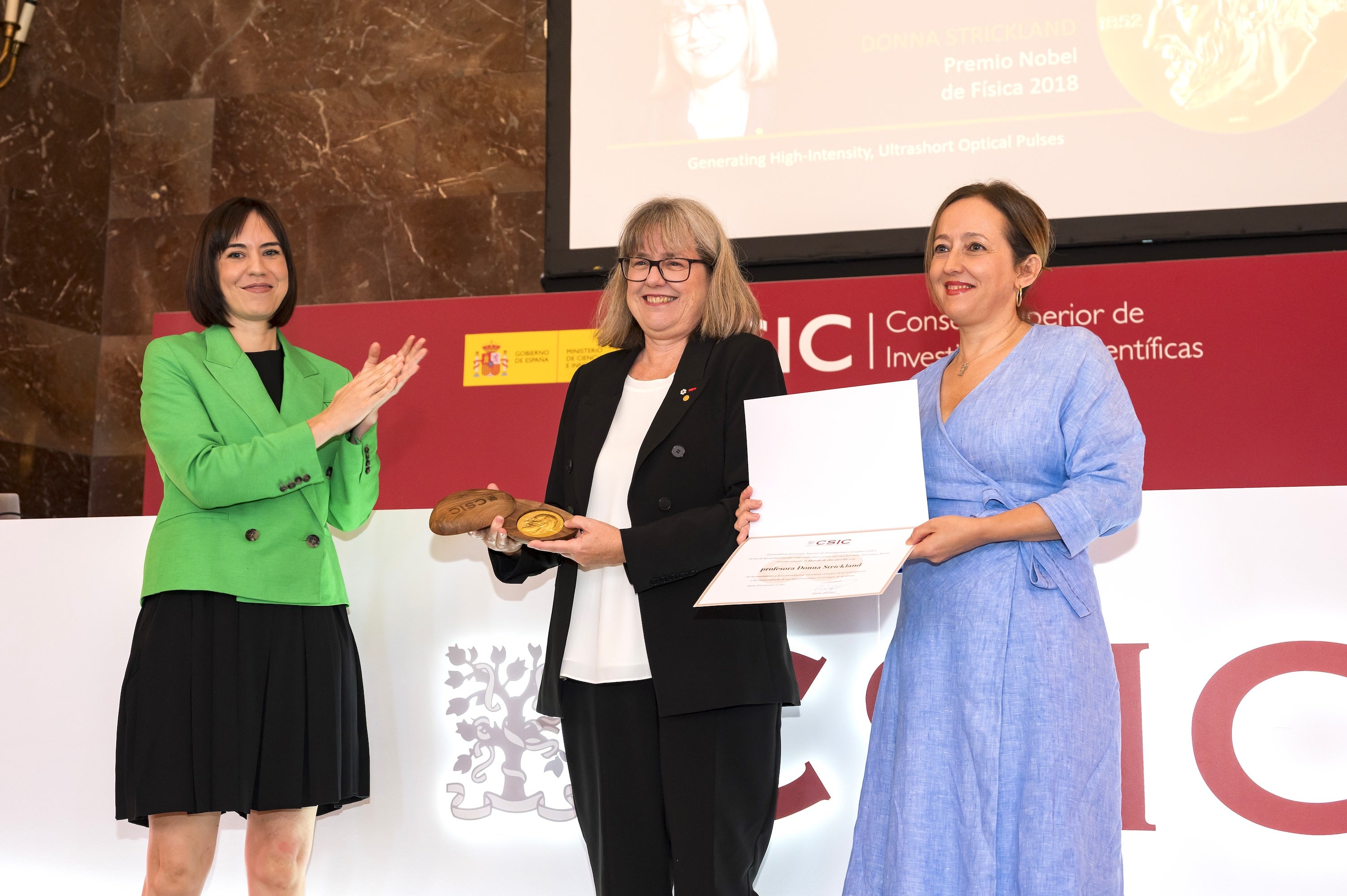 Image of Noble Prize Winner, Donna Strickland, receiving Gold Medal from the acting minister of science and innovation, Diana Morant, and the president of the CSIC, Eloisa del Pino.