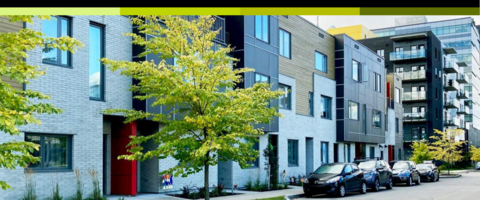 A wide shot of a 3-storey apartment building with cars parked in front. 