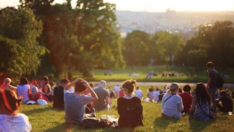 Wideshot of young adults sitting on a hill in a park overlooking a cityscape.