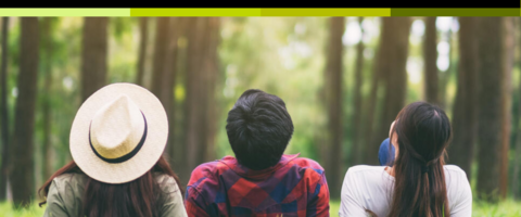 A wide shot of 3 young people lying on a forest floor and looking up into the sky.