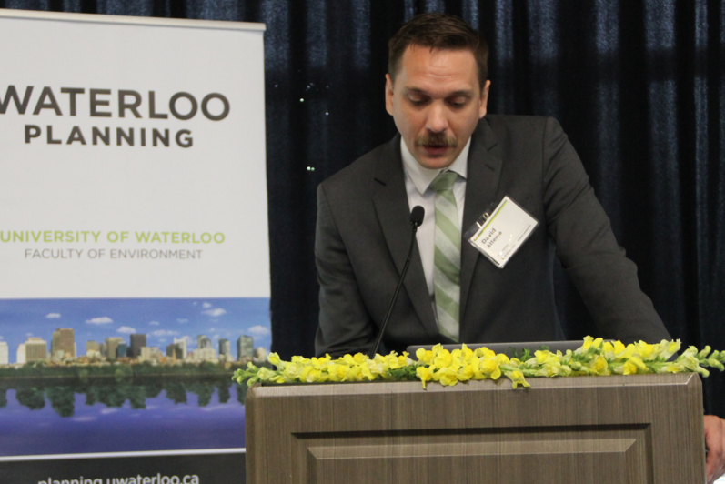 2024 Graduate Luncheon Graduate Speaker David Attema presenting in front of a podium and School of Planning banner.