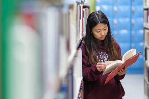 A student reads through a book standing amongst the stacks in the Dana Porter Library