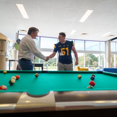 Bill Shaking hands with a student near a pool table