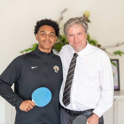 Bill standing with a student holding a ping pong paddle 