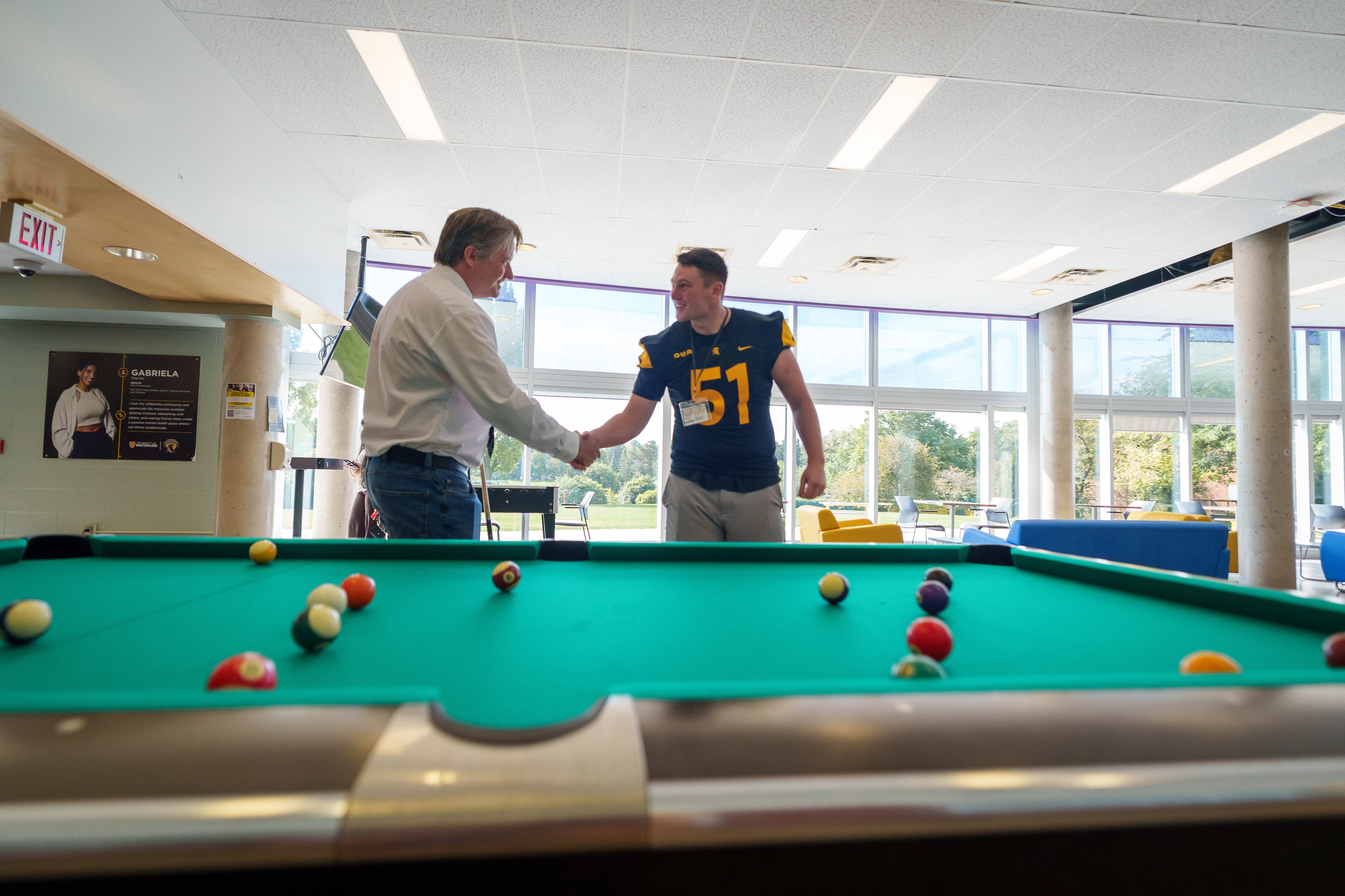 Bill Shaking hands with a student near a pool table