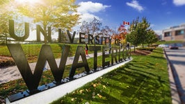Sunshine cascades across the University of Waterloo sign on a fall day with leaves on the ground