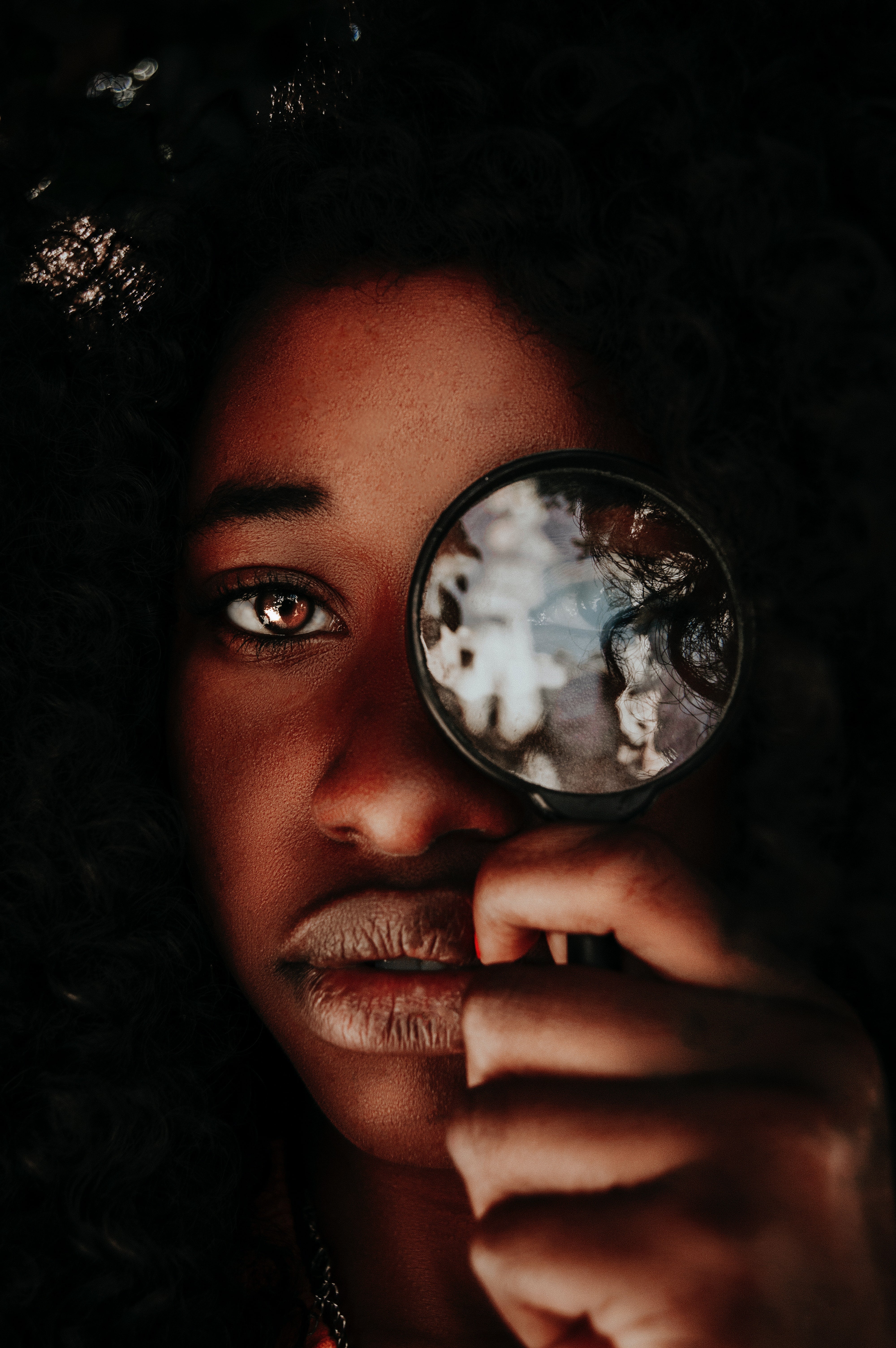 Black woman holding a magnifying glass up to her left eye