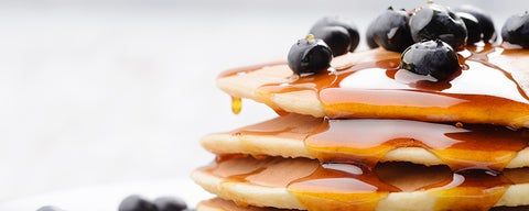 Stack of pancakes dripping in syrup and covered with blueberries.