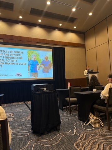 Hannah Johnson standing on a podium presenting her research with the title slide displayed.