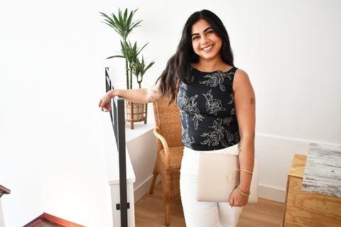 Sucheta Khurana holding a laptop and leaning on a stair banister while smiling warmly at the camera