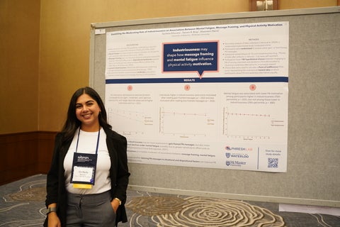Sucheta Khurana standing in front of her poster smiling at the camera.
