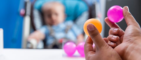 An infant being shown a small orange ball and a small pink ball