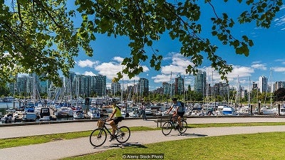 two cyclist riding along water front with marina and city in background