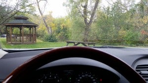 sitting in a car, behind the steering wheel looking out at a gazebo in the park
