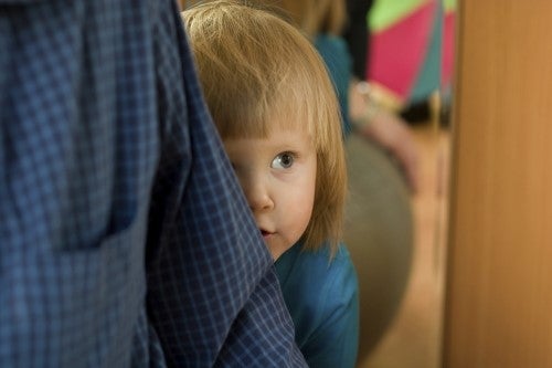 shy toddler hiding behind parent