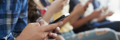 Several teens sit with their smartphones in their hands.