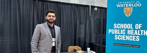 Harris Manzoor wearing a suit and standing at a conference booth.