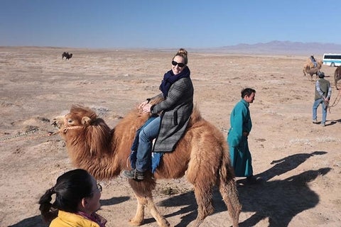 Lesley Johnson rides camel in the desert.