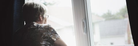 Elderly woman peers out a window on a gloomy day.