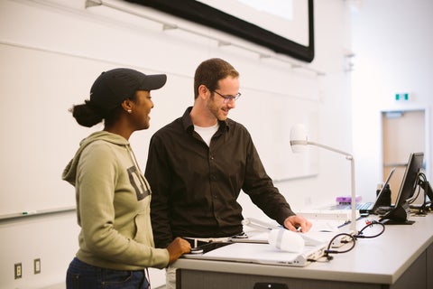 Instructor at lecture podium explaining concept to a student.