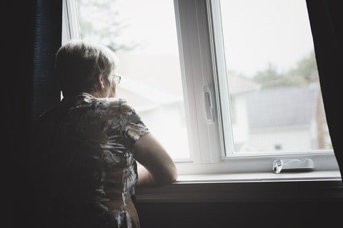 Elderly woman peers out a window on a gloomy day.