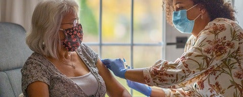 Nurse wearing mask vaccinates older adult.