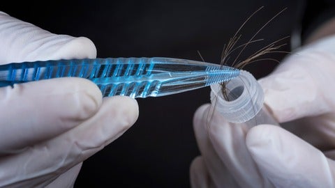 Researcher's gloved hands using tweazers to put hair strands in test tube.