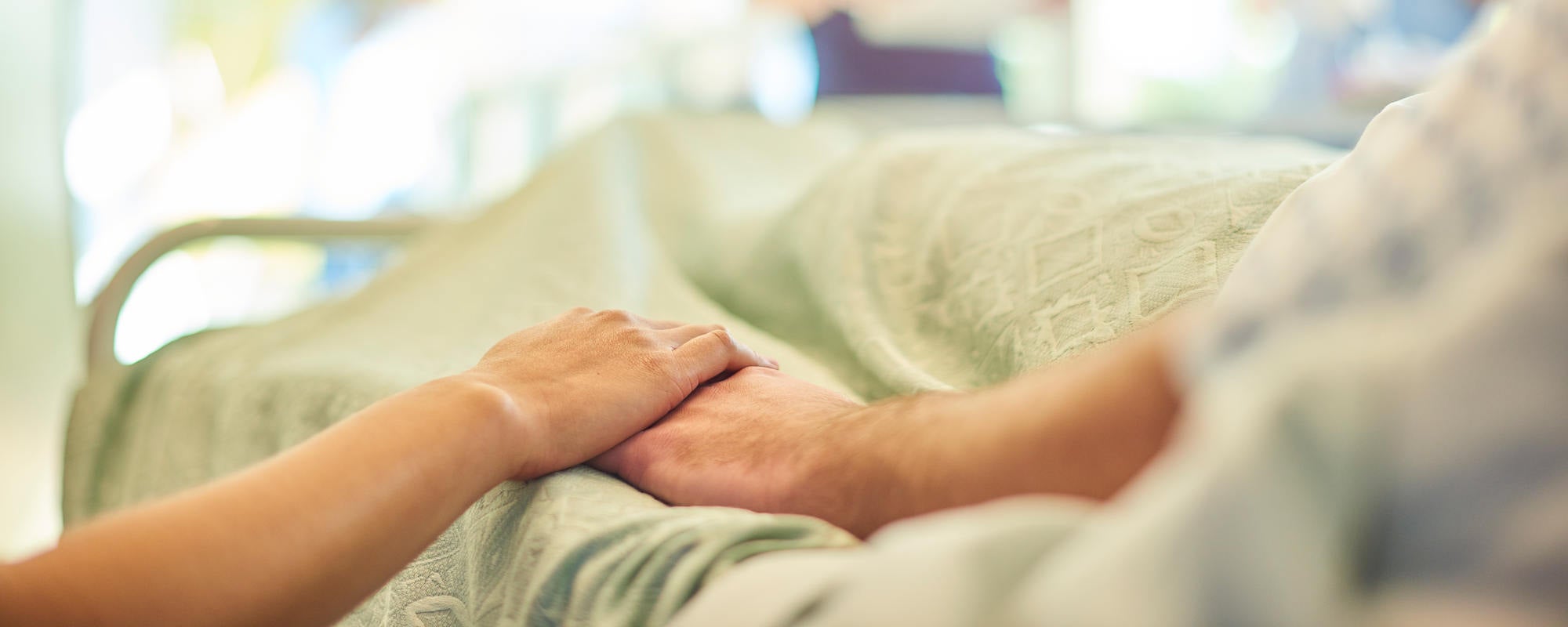 Person holding hands with someone in a hospital bed