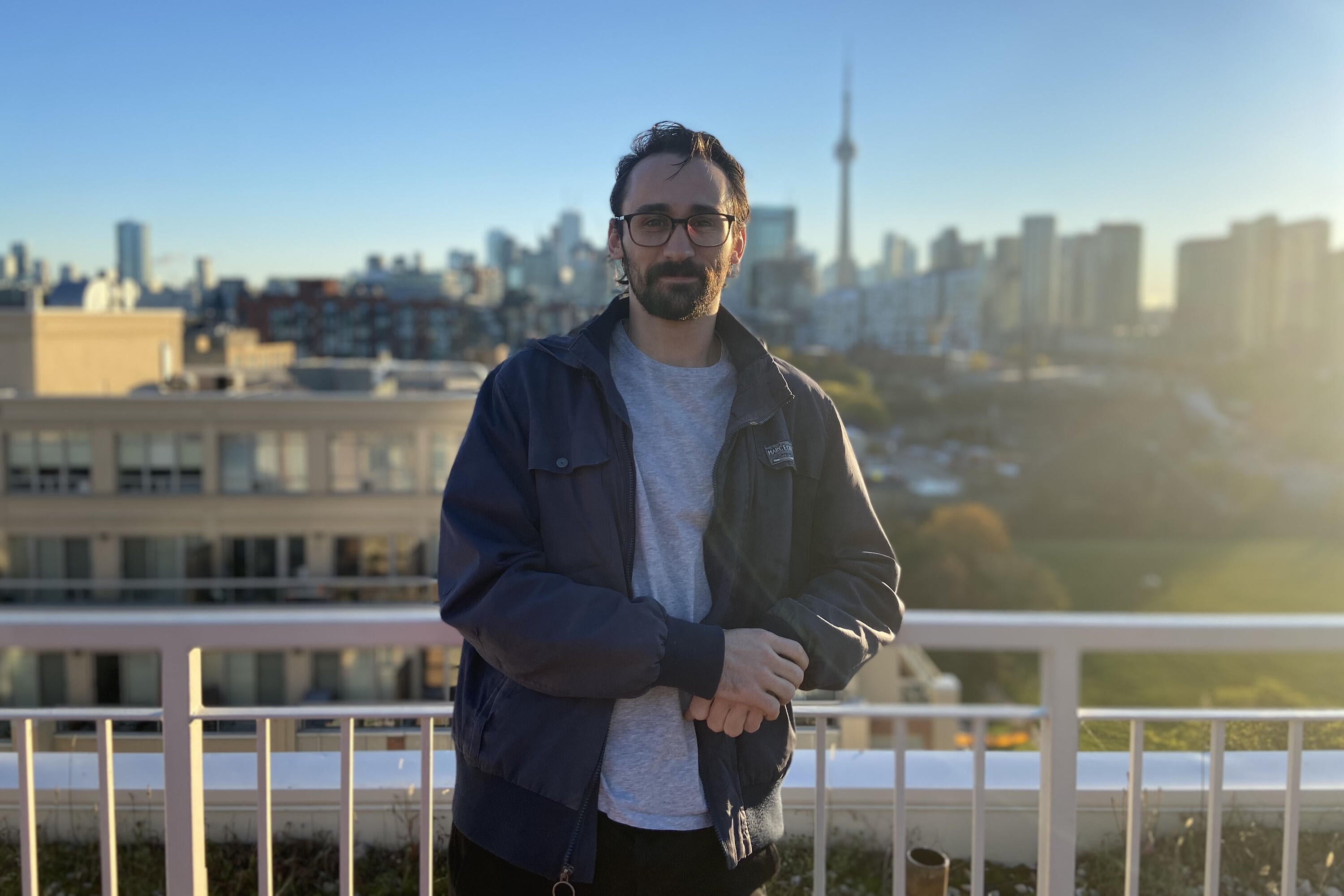 Brendan Flynn standing on a rooftop deck in Toronto with CN tower in the distance.