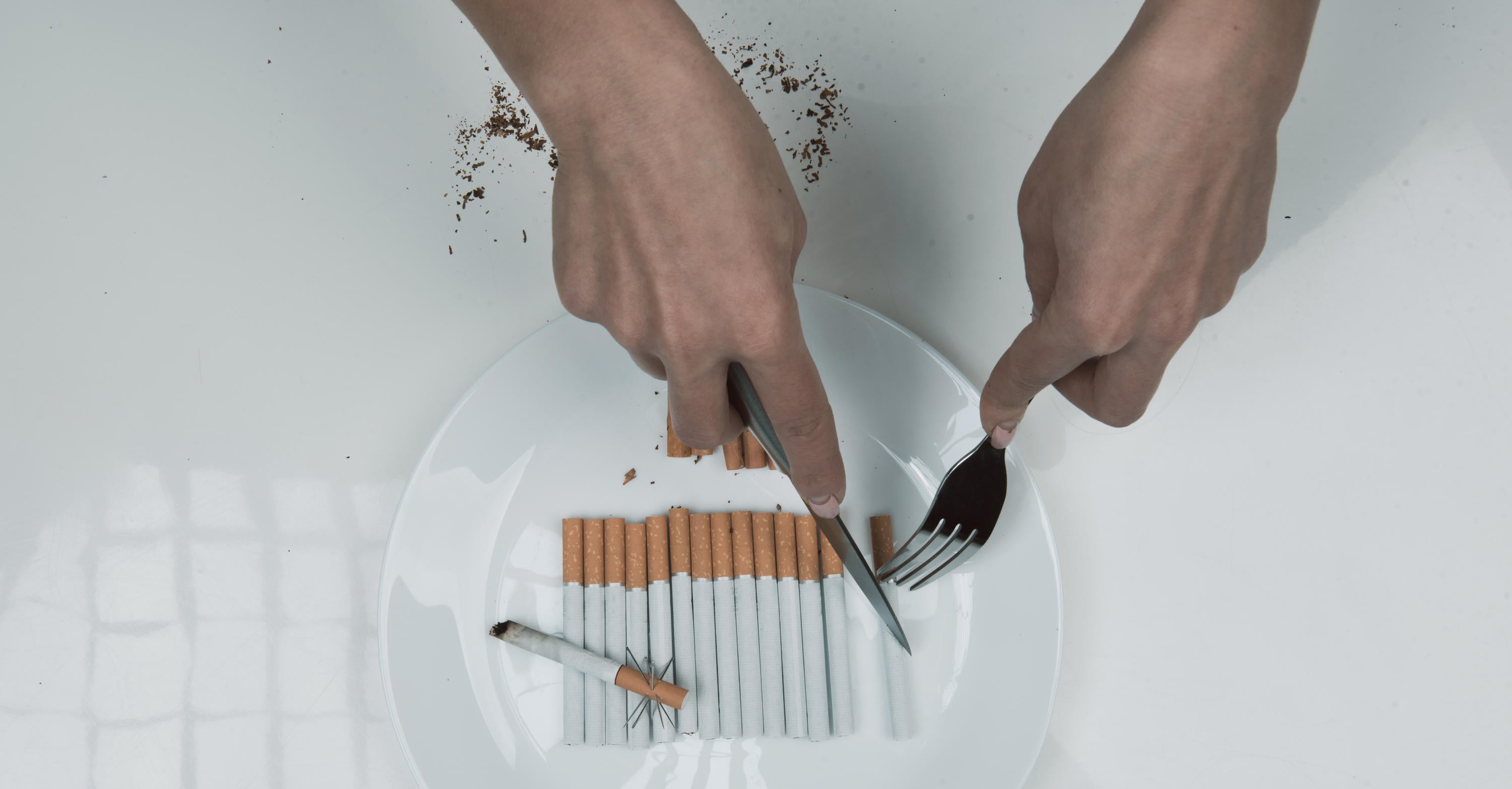 hands using knife and fork to cut cigarettes on a plate