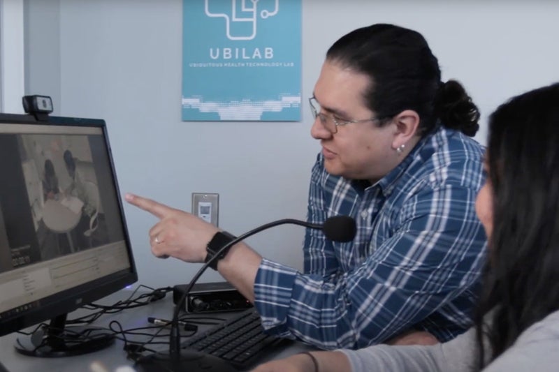 Professor and student examine health informatics research on a computer monitor.