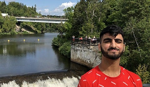 Gurtaj Dhaliwal in front of a bridge over a river