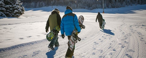 Three snowboarders walking on wintery path.