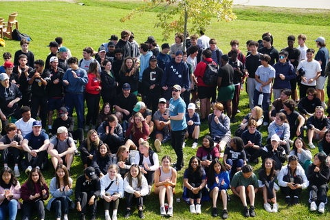 large group of students sitting on grass smiling for photo 