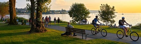 Young couple cycling, others walking or jogging at sunset in city park.