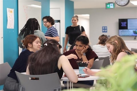 Graduate students engaging in group study work and recreational activities in communal working area.