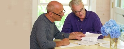 Two older men sit at table reviewing documents.