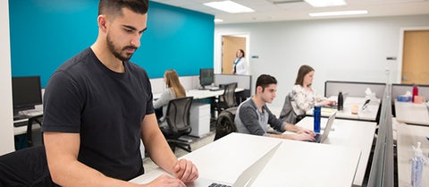 Graduate student works on laptop at standing desk.