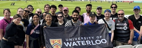 Recreation and Leisure Studies Students on a recreation field in London, England, holding a University of Waterloo banner.