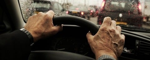Hands grip car steering wheel in traffic.