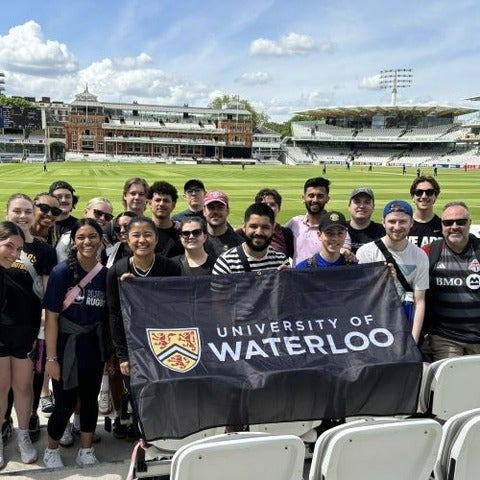 Recreation and Leisure Studies Students on a recreation field in London, England, holding a University of Waterloo banner.