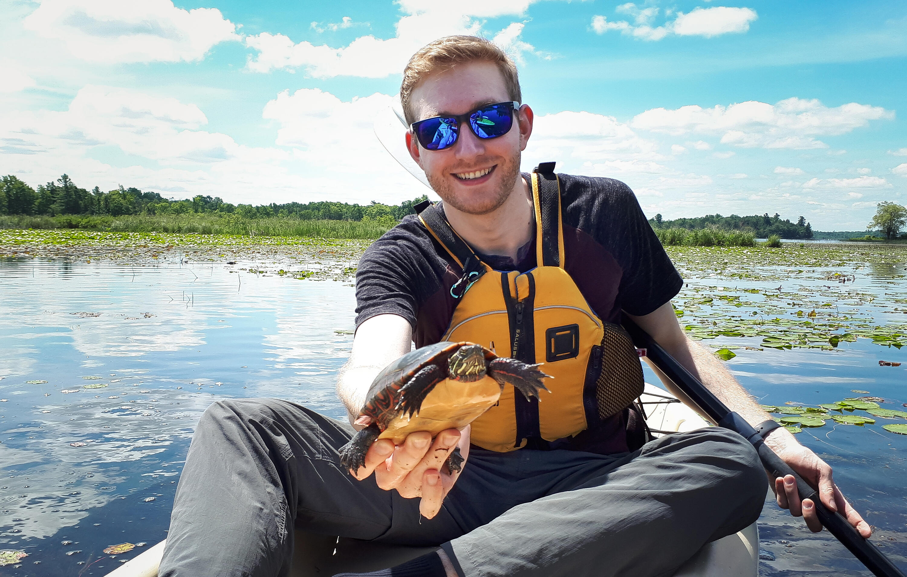 Andrew McDonald sitting in a kayak holding a turtle and smiling.