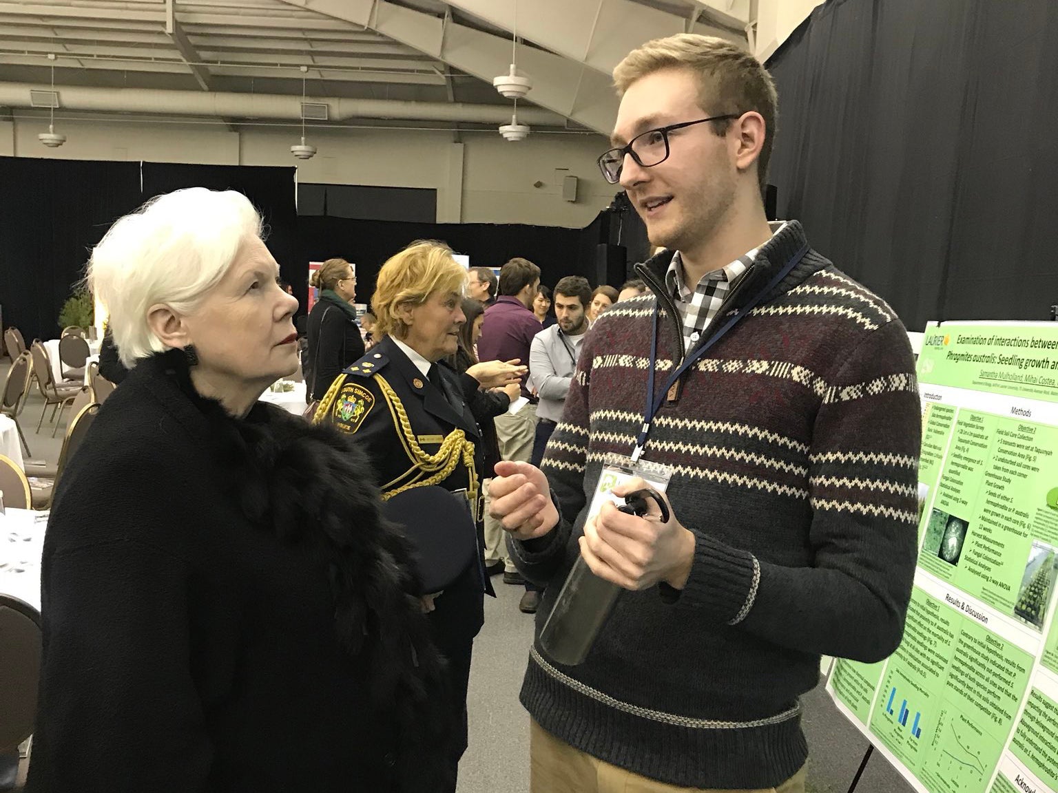 Andrew McDonald talking to a lady with silver hair at an event in front of his research poster.